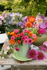 Colourful zinnias hydrangea and dahlia flowers in jugs and bowl   on a table outdoors in a garden