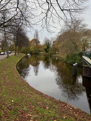 Obraz premium Beautiful view of canal with moored boat and colorful fallen leaves on autumn day