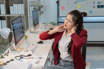 Young office worker massaging her neck, suffering from chronic pain after long hours working on...