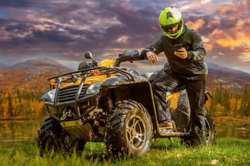 Man near ATV. Guy with phone and dirty mod SUV. ATV for off-road driving. ATV driver builds route in mobile application. Men extreme sportsman and quad bike in wild. Quad bike to ride through forest © Grispb
