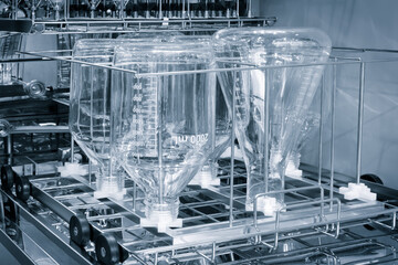 A rack of glassware is in a dishwasher. The glassware is in a rack with a basket underneath medical...