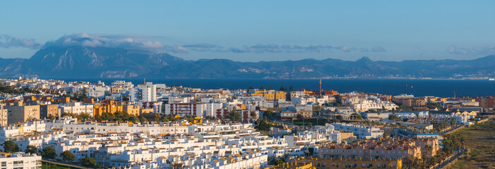 Aerial view of Tarifa, Spain, featuring Andalusian architecture, the Strait of Gibraltar, and distant Moroccan mountains under a clear blue sky.