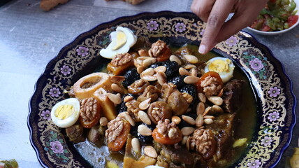 Traditional Moroccan Meat with Prunes, Nuts, and Boiled Eggs in Ornate Peacock Platter – Authentic North African Cuisine for Festive Occasions  

