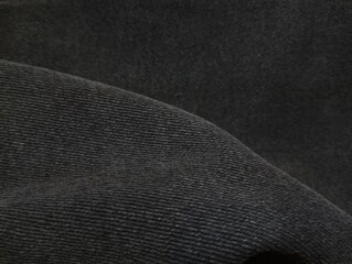 Background of dark gray jeans with a diagonal fold. Background of denim fabric.