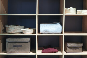 A wooden shelf with a variety of baskets and boxes. A white towel is on the top shelf