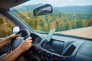 The man's hands on the steering wheel of the car. Driving on a dirt road in autumn.