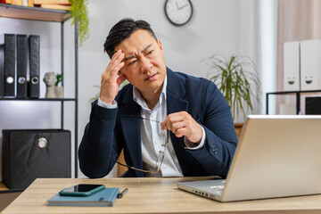 Naklejka premium Tired Asian businessman feeling worried about financial problem stress at home office workplace. Middle-aged freelancer broker man frustrated thinking of money debt budget loss bankruptcy. Overworking