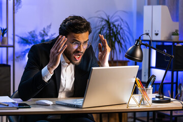 Irritated tired Indian business man while working on laptop, unexpected online website problem,...