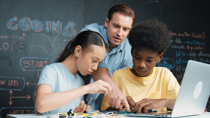 Caucasian teacher talking about electric tool while student fixing robotic model on table with...