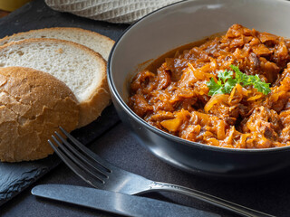 Polish vegetarian bigos, boiled sauerkraut with tomatoes and fried smoked tofu. Served in a bowl with bread.