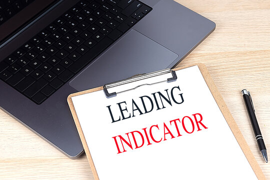 Clipboard with the text leading indicator on a desk with a laptop and black pen