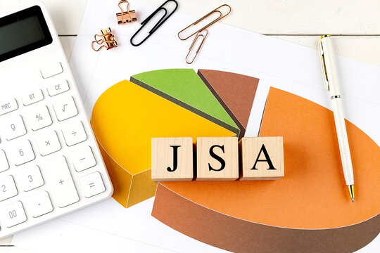 Wooden blocks with JSA text on a colorful pie chart with a calculator, paper clips, and a white pen