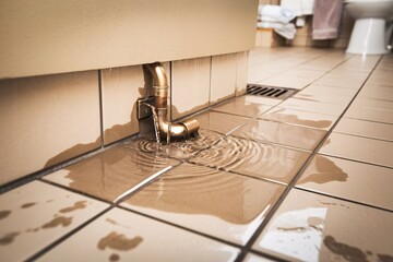 A photo of water seeping from a broken pipe joint on a tiled bathroom floor 