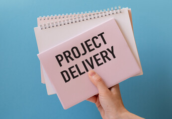 PROJECT DELIVERY text on a notebook on blue background
