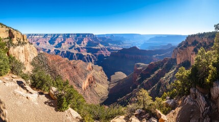 Naklejka premium Panoramic view of Grand Canyon's vastness, showcasing layered rock formations, deep canyons, and desert vegetation under a clear blue sky.