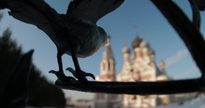 Religion, architecture. The figure of a bird in a wrought-iron fence against the background of a Christian temple is out of focus on a cold day. Hand held, distortion . Siberia.