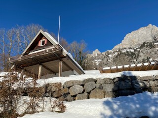 Fototapeta premium Old traditional swiss rural architecture and alpine livestock farms in the winter ambience over the Lake Walen or Lake Walenstadt (Walensee) and in Swiss Alps, Walenstadtberg - Switzerland (Schweiz)