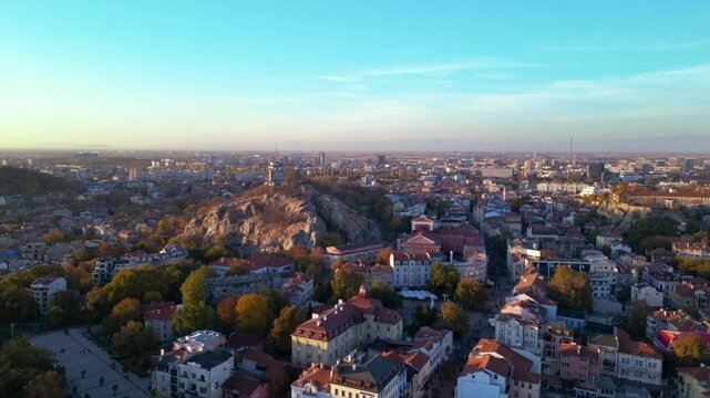 Aerial drone footage of a sunset over the city of Plovdiv in Bulgaria. Ancient city of Filipopolis filmed from above on a warm autumn afternoon. European city seen from a helicopter establishing shot.