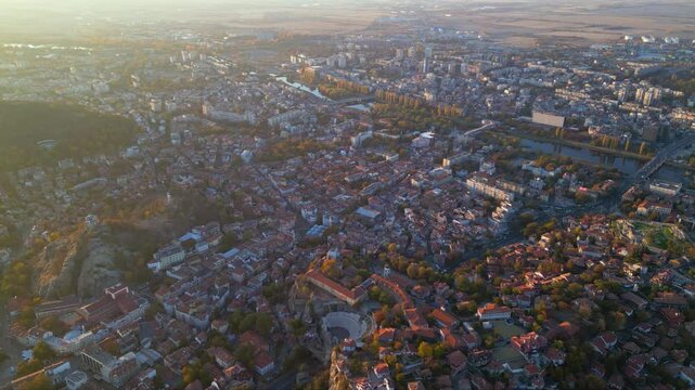 Aerial drone footage of a sunset over the city of Plovdiv in Bulgaria. Ancient city of Filipopolis filmed from above on a warm autumn afternoon. European city seen from a helicopter establishing shot.