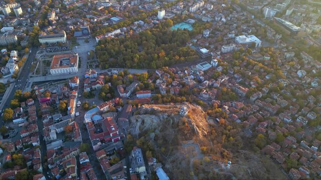 Aerial drone footage of a sunset over the city of Plovdiv in Bulgaria. Ancient city of Filipopolis filmed from above on a warm autumn afternoon. European city seen from a helicopter establishing shot.