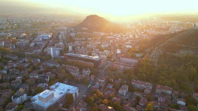 Aerial drone footage of a sunset over the city of Plovdiv in Bulgaria. Ancient city of Filipopolis filmed from above on a warm autumn afternoon. European city seen from a helicopter establishing shot.
