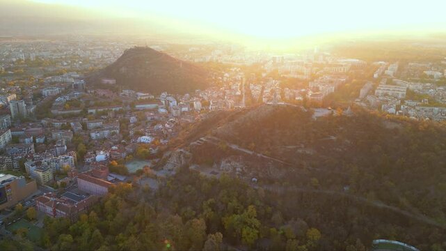 Aerial drone footage of a sunset over the city of Plovdiv in Bulgaria. Ancient city of Filipopolis filmed from above on a warm autumn afternoon. European city seen from a helicopter establishing shot.
