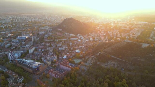 Aerial drone footage of a sunset over the city of Plovdiv in Bulgaria. Ancient city of Filipopolis filmed from above on a warm autumn afternoon. European city seen from a helicopter establishing shot.