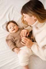 Happy mother holding baby girl 5-6 months old lying in bed at home close up. Motherhood.