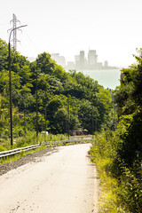 A paved road winds through a lush, green forested area. Batumi skyline is visible on the horizon.