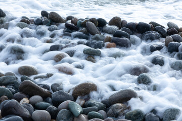 Obraz premium Smooth, rounded stones are scattered on a beach with water flowing over them from ocean waves. The stones vary in size and color, adding visual interest and texture.