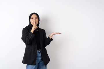 Asian muslim women with black hijab and suit put finger in front of her mouth telling quite sign with open palm presenting copy space and face looking to camera
