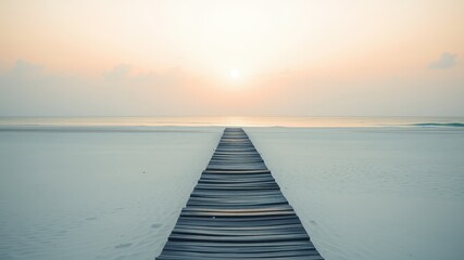 Fototapeta premium A Wooden Pathway Leads to the Horizon Across a Pristine Beach Under a Clear, Pale Sky