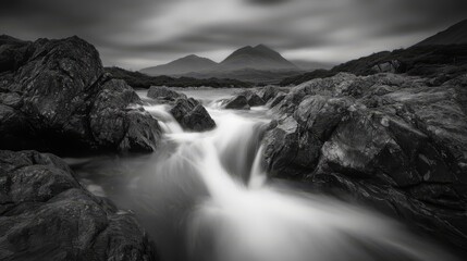 Dramatic black and white long exposure of a cascading river flowing between dark rocks, with mountains in the background under a moody sky.