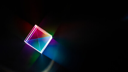 A glass dichroic prism disperse light into different colors on a black background