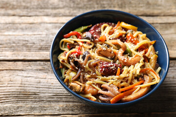 Stir-fry noodles with sea food and vegetables on wooden table, closeup. Space for text