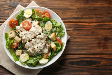 Tasty Caesar salad with chicken and tomatoes in bowl on wooden table, top view. Space for text