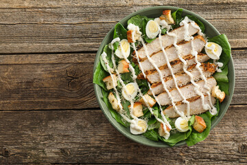 Delicious Caesar salad with chicken on wooden table, top view. Space for text