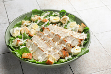 Delicious Caesar salad with chicken on textured tiled table, closeup