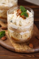 Tasty trifle dessert. Sponge cake, banana and whipped cream in glass on wooden table, closeup