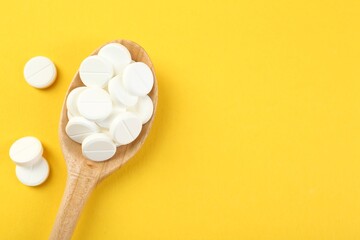 Antibiotic pills in spoon on yellow background, top view. Space for text