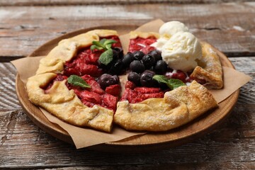 Tasty galette with berries, ice cream and mint on wooden table, closeup