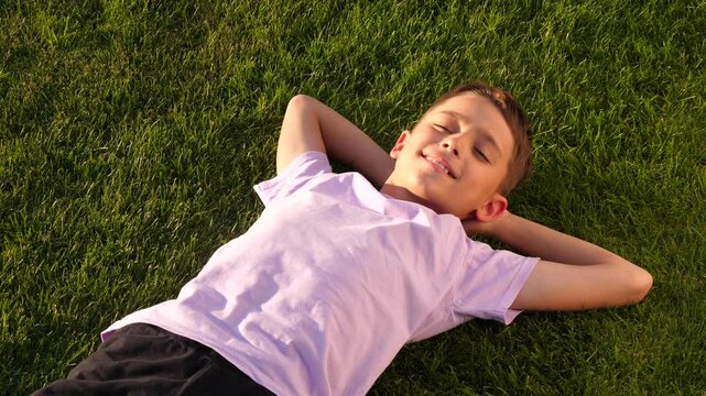 happy face boy lie in grass. joyful boy smiling lying relaxation sunny day green park. dreamy boy