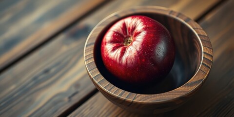 A single, ripe red apple sits nestled in a wooden bowl, its surface glistening with moisture, ready for a delicious bite.