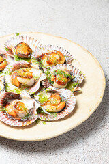 A close-up of grilled scallops served in their shells, garnished with green herb sauce, displayed on a beige ceramic plate on a textured surface
