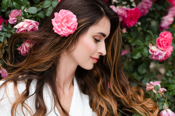 Naklejka premium Beautiful young woman 25-29 year old with long blonde hair posing with pink rose flowers in garden outdoors. Springtime.