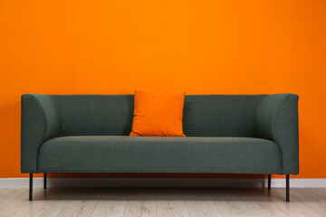 Stylish sofa with pillow near orange wall indoors