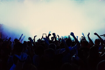 Rear view Silhouette of a crowd with their arms in the air at a concert