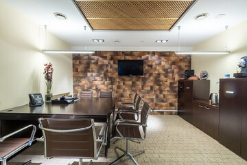A sleek office space showcases a large dark wooden desk surrounded by stylish leather chairs. A wall-mounted television enhances the modern design
