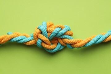 Colorful ropes tied in knot on light green background, top view. Unity concept