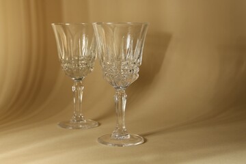 Two empty wine glasses on beige background, space for text